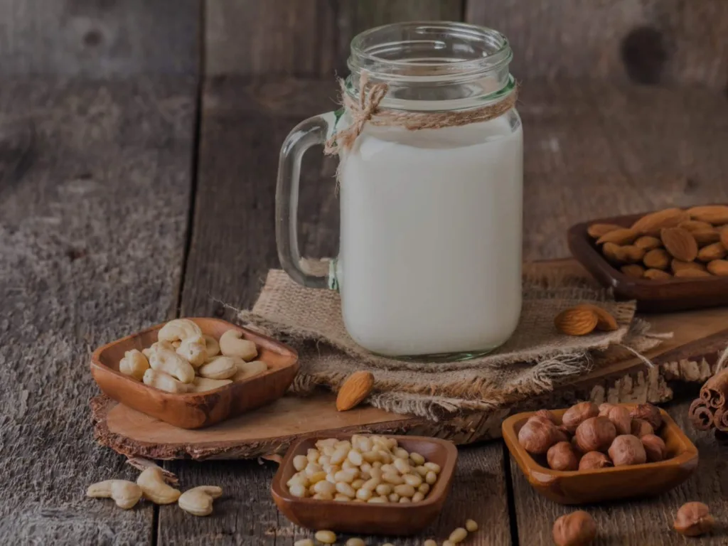 Organic nut milk in a glass jar and cashews, almonds and hazelnuts in small bowls